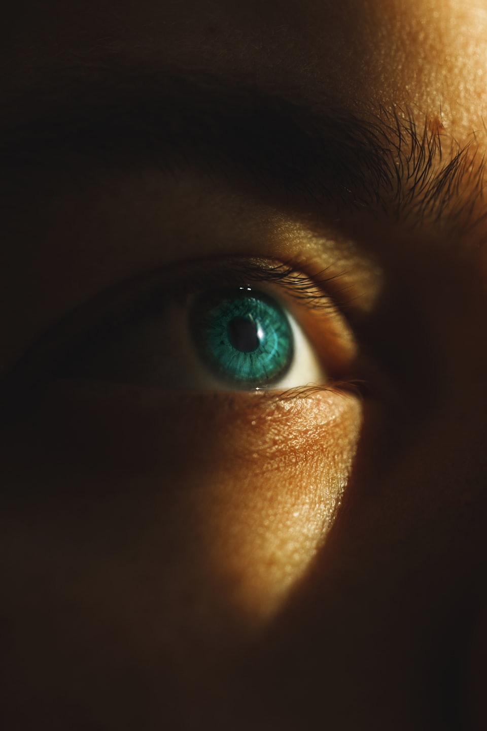 a closeup image of a turquoise coloured human eye iris. Much of the portrait is in shade with a light purposefully highlighting the eye itself. Eyes of Britain. Iris photography. Eye photography. Photography project. UK